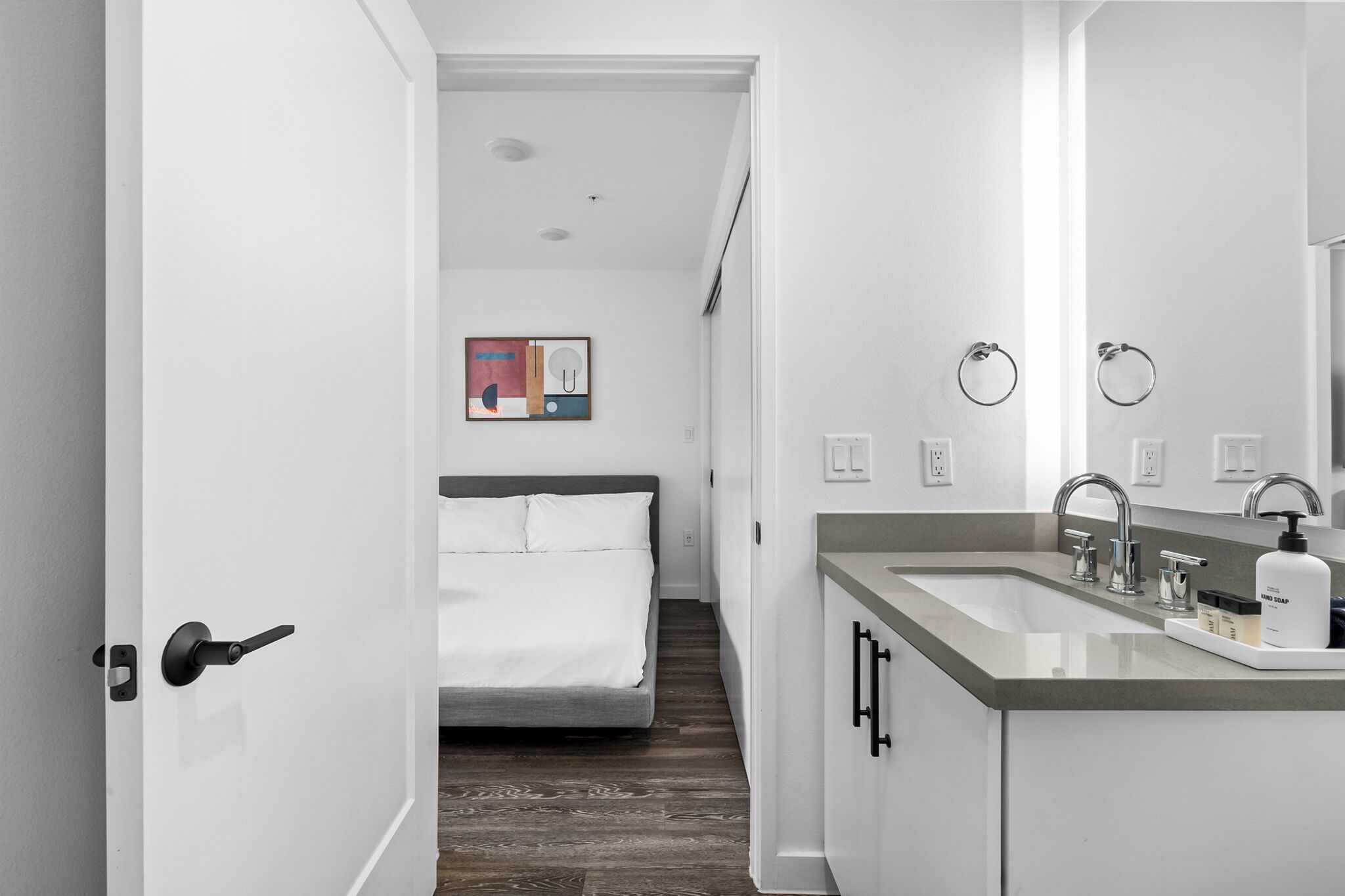 A modern bathroom with a sink, mirror, and towel rings.