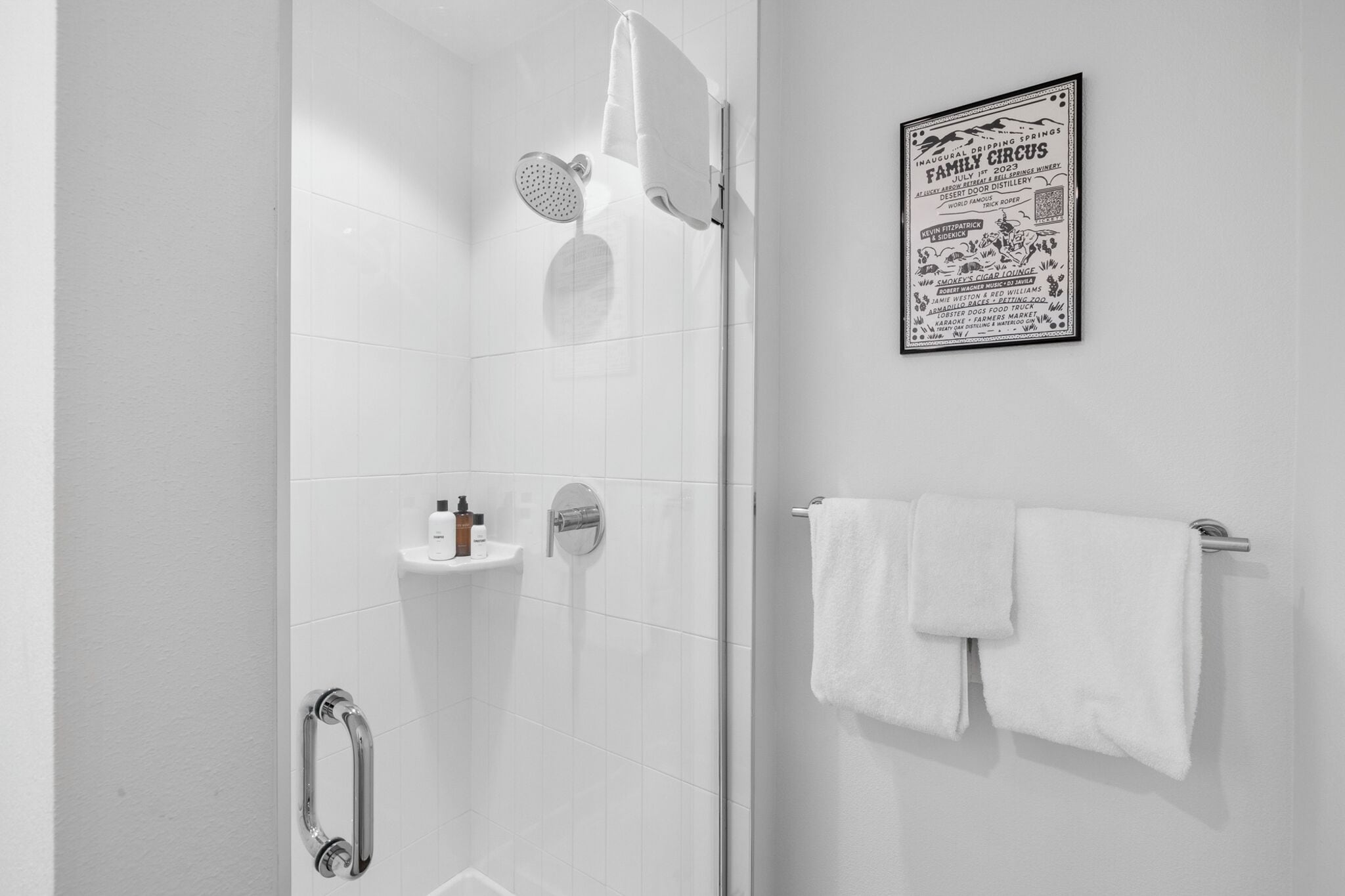 Une salle de bain moderne avec une douche à parois de verre, une barre d’appui, un porte-serviettes et une affiche accrochée au mur.