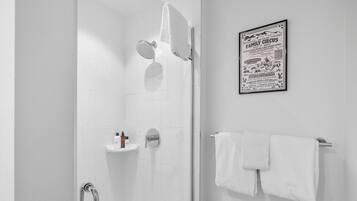 Une salle de bain moderne avec une douche à parois de verre, une barre d’appui, un porte-serviettes et une affiche accrochée au mur.