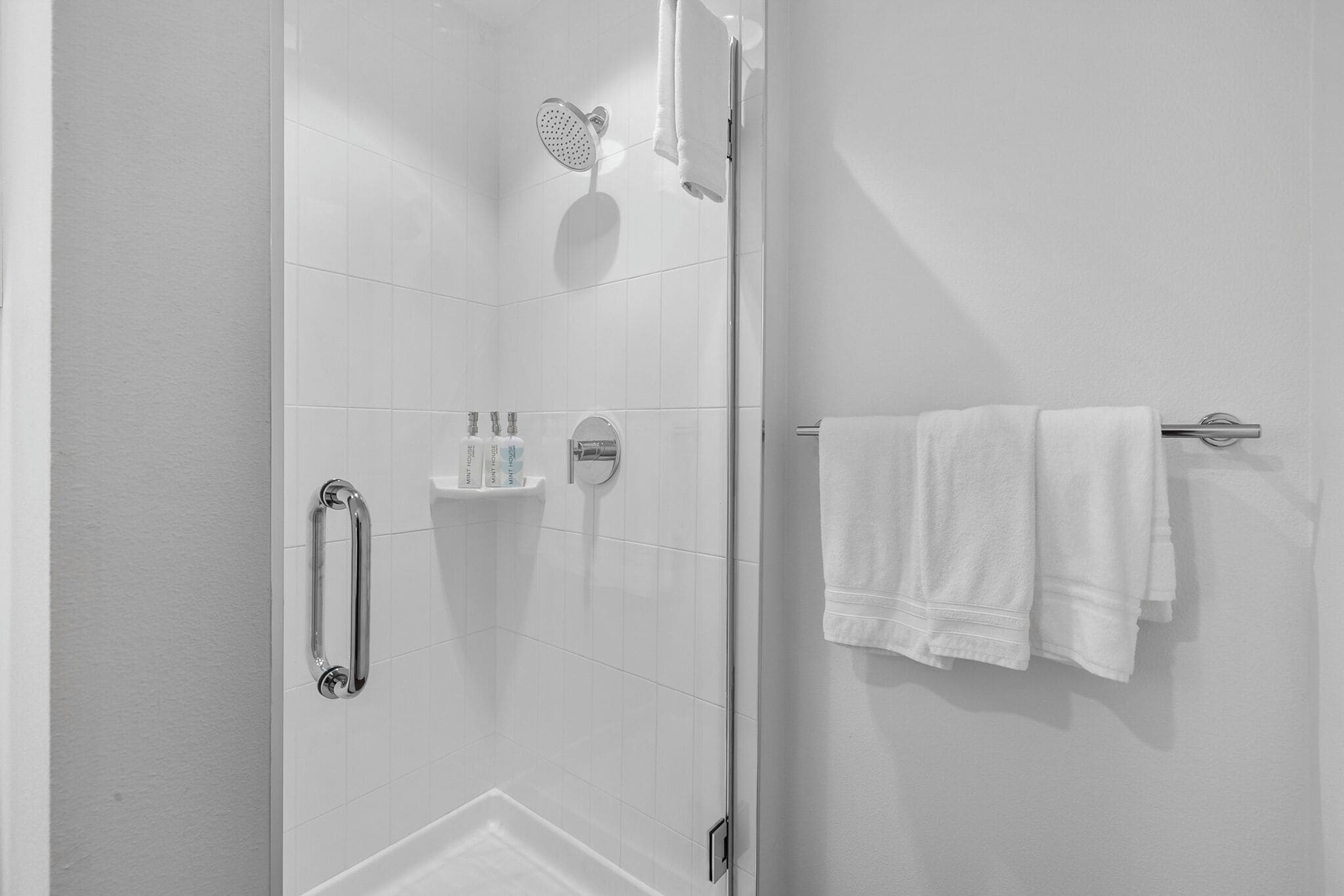 Um banheiro moderno com box de vidro, porta-toalhas branco e prateleira com artigos de higiene pessoal.