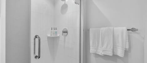 A modern bathroom with a glass shower enclosure, a white towel rack, and a shelf with toiletries.