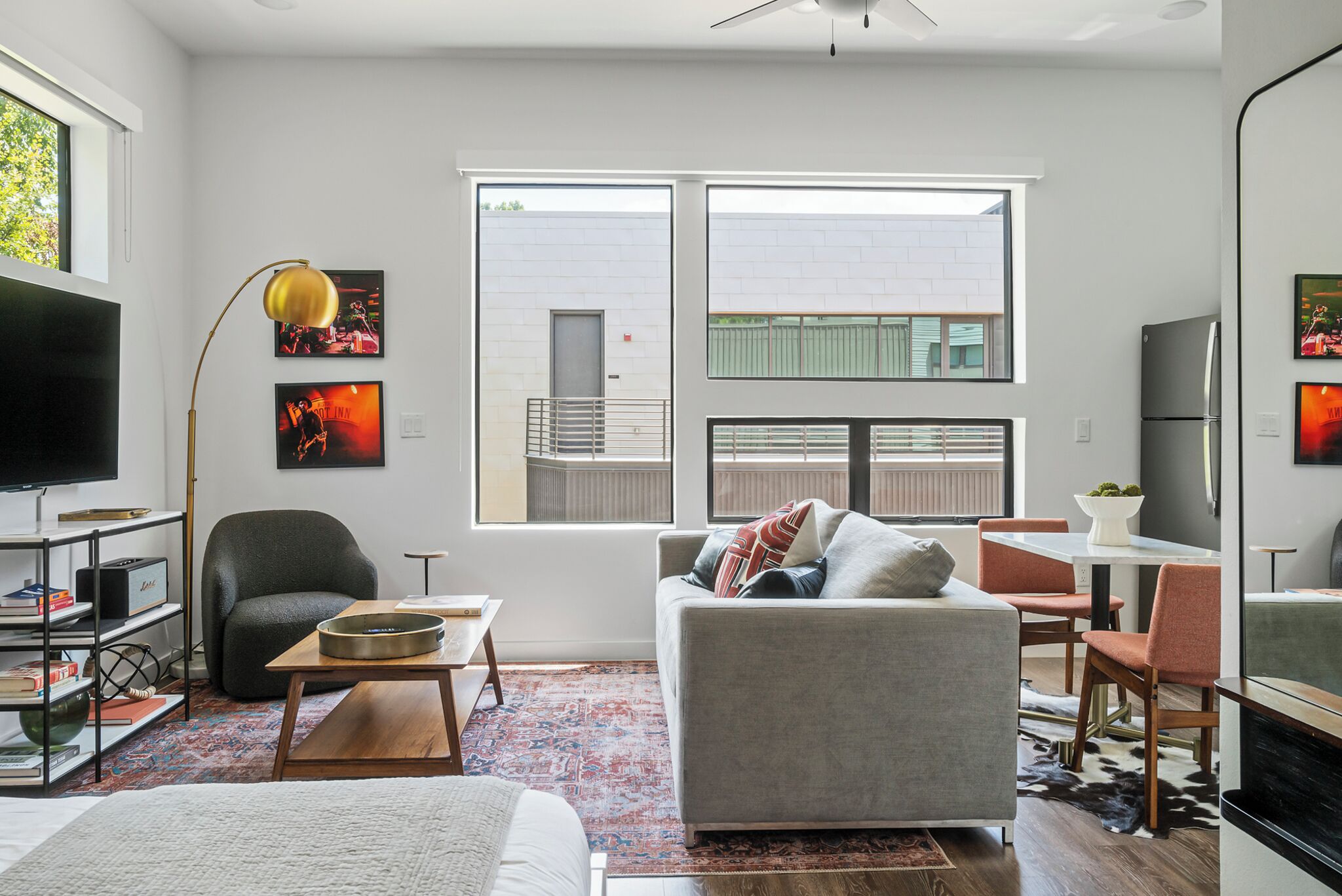 A modern living room with a sofa, coffee table, and a TV. There are two windows with a view of a building outside.