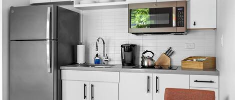A modern kitchen with white cabinets, a stainless steel refrigerator, a microwave, a coffee maker, and a kettle.