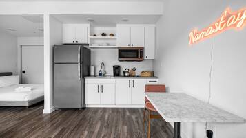 Una cocina moderna con armarios blancos, un refrigerador de acero inoxidable, un microondas y un letrero de neón.