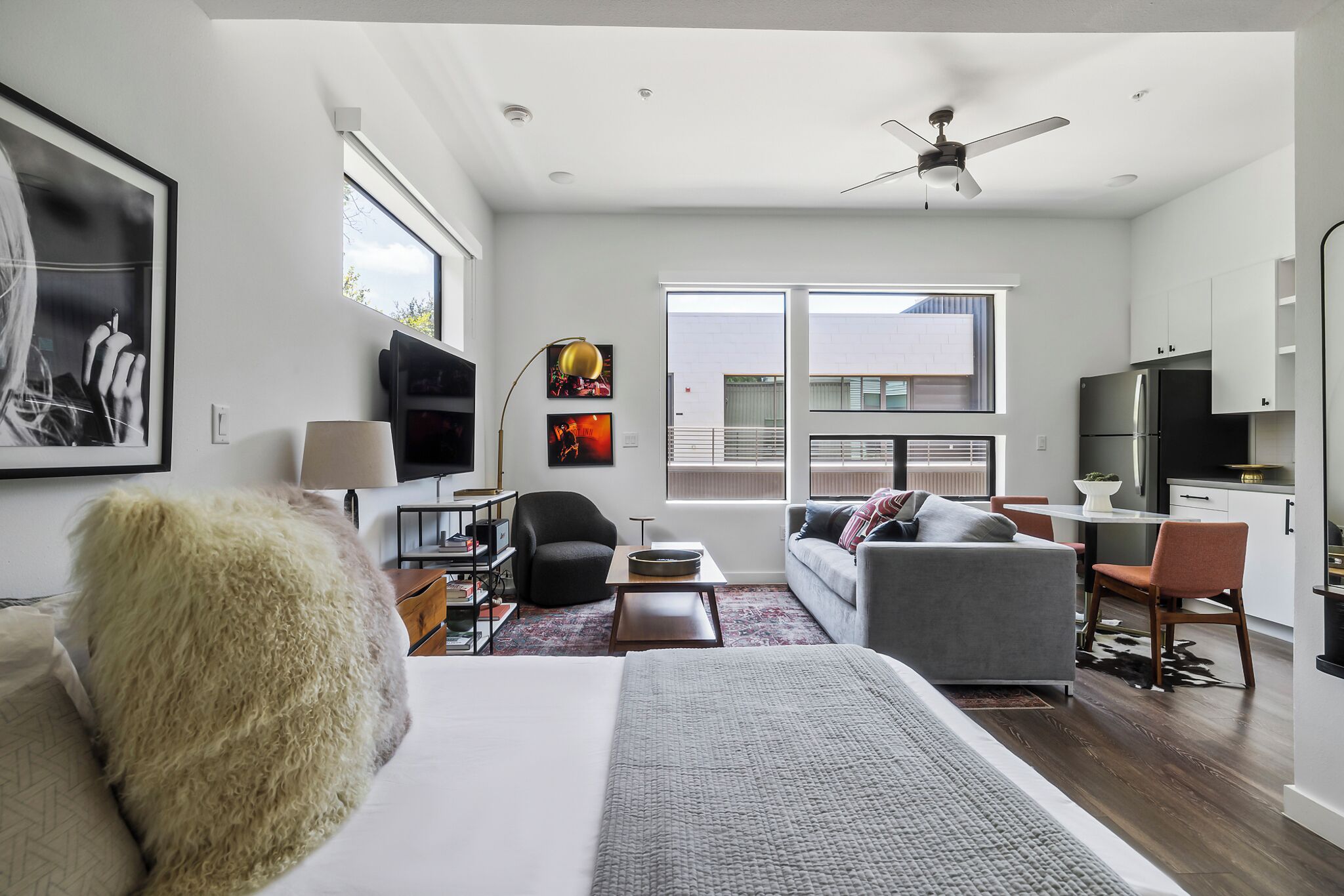 A modern hotel room with a large bed, a sofa, a desk, and a TV. There is a balcony with a view of the city.