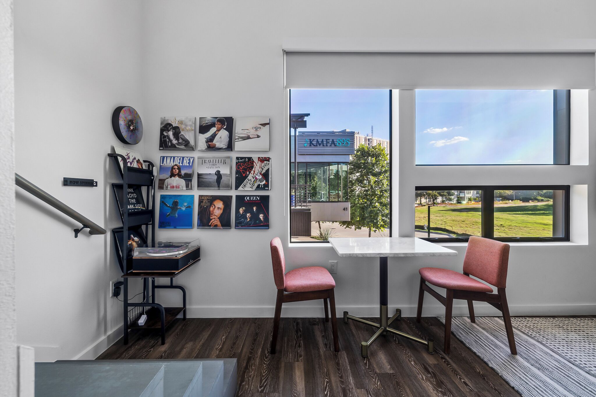 A modern room with a large window, a desk with a chair, and various posters on the wall.