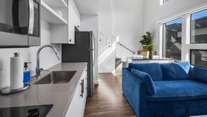 A modern kitchen with a built-in oven, a sink, and a countertop. There is a blue sofa and a staircase leading to an upper level. - Holly House (Austin)