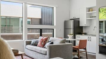 A modern, well-lit room with a grey sofa, a dining table, and a kitchen area with white cabinets and a refrigerator.