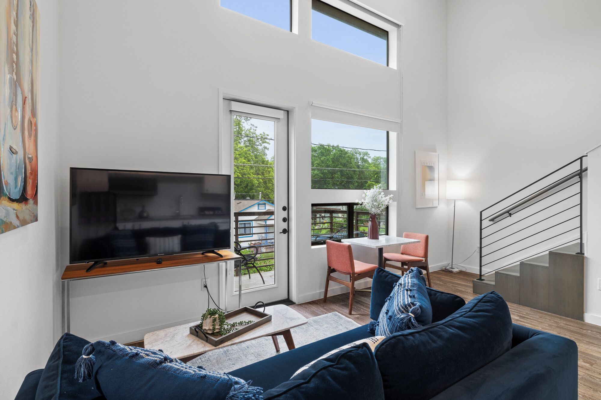 Una sala de estar moderna con un televisor de pantalla plana, un sofá, una zona de comedor con sillas y una escalera.
