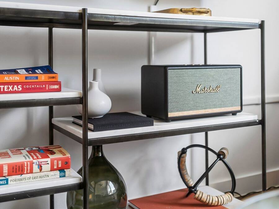 Una estantería con libros, un jarrón, una lámpara y un altavoz Marshall.