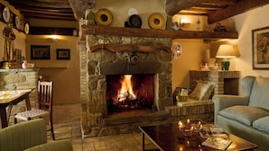 Un salon chaleureux avec une cheminée en pierre, un canapé confortable, une table basse avec des bougies et un plafond en bois rustique.