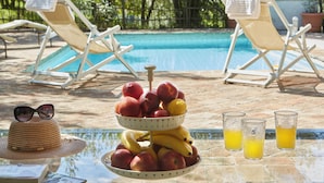 Un espace aménagé au bord de la piscine, avec des chaises longues, un panier de fruits et des verres de jus d’orange.