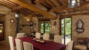 Une salle à manger rustique avec un plafond en bois, des murs en pierre et une table dressée avec une nappe rouge et des chaises blanches.