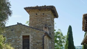 Un bâtiment en pierre avec un petit escalier menant à une porte, entouré de verdure et sous un ciel dégagé.