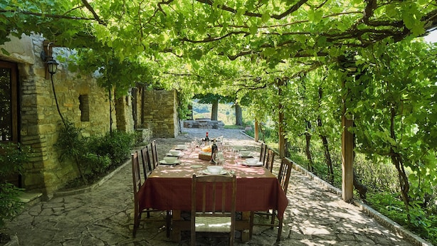 Un espace de restauration en plein air avec un sol en pierre, des chaises en bois et une table dressée pour un repas.