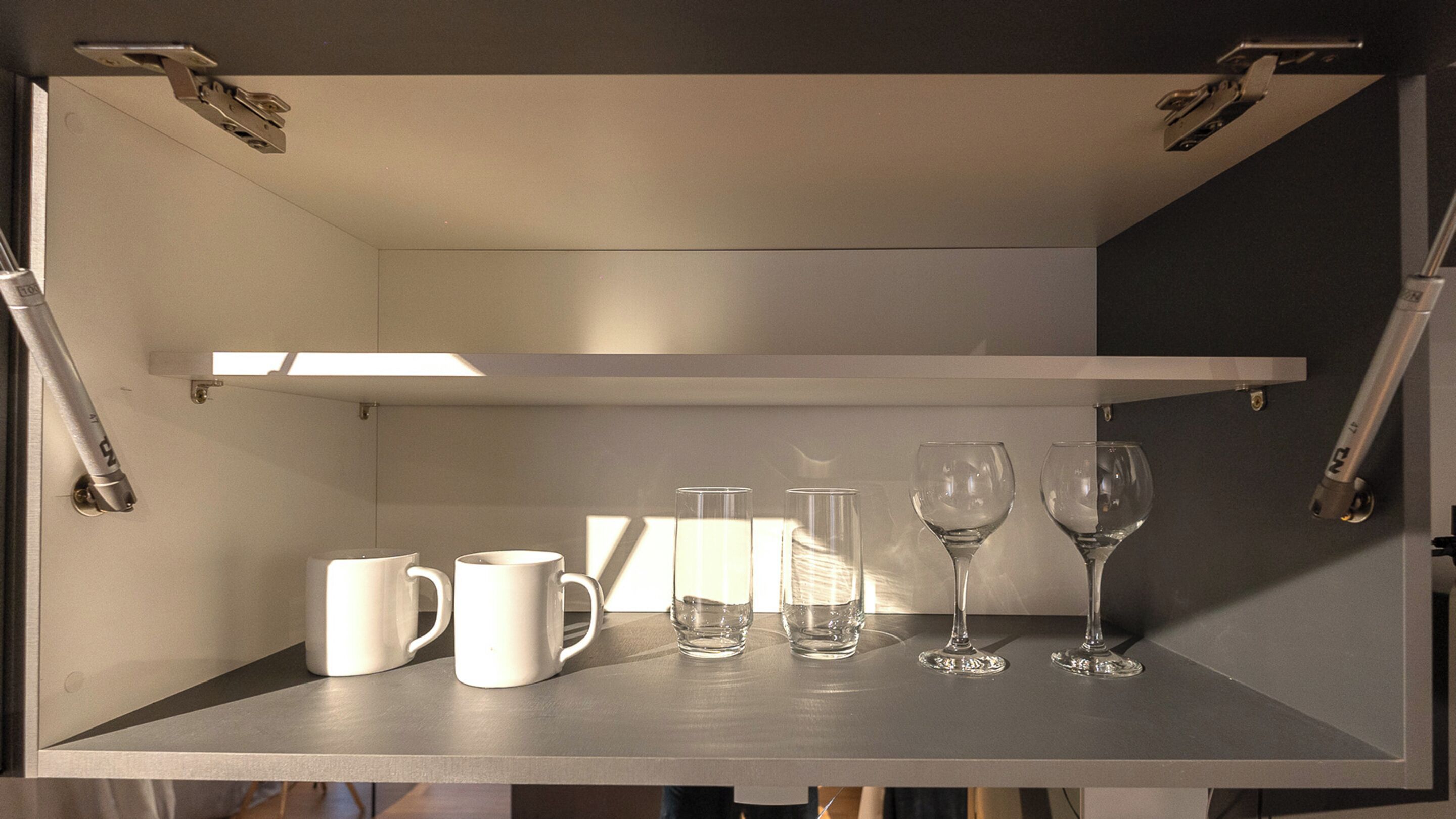 A shelf with white mugs and clear glasses.