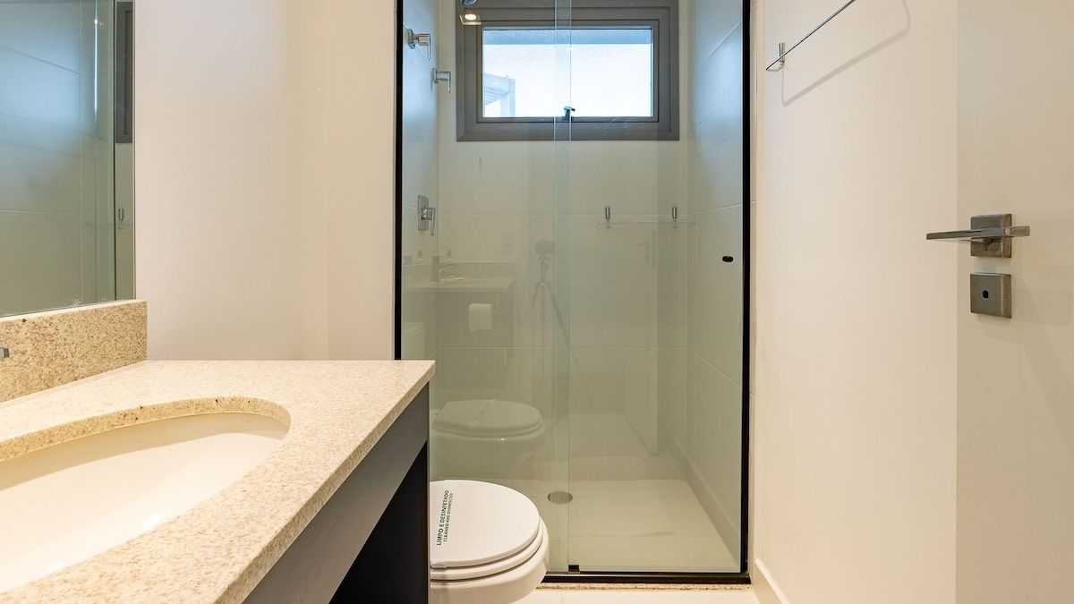 A modern bathroom with a glass-enclosed shower, a white toilet, and a granite countertop.