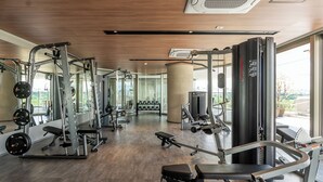 Une salle de sport moderne dotée de divers appareils d’exercice, de grandes fenêtres et d’un plafond en bois.
