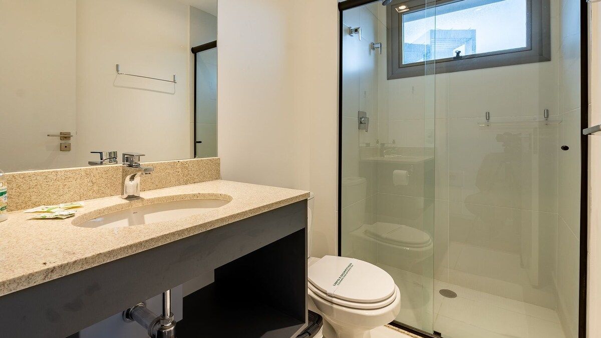 A modern bathroom with a glass-enclosed shower, a sink with a granite countertop, and a toilet.