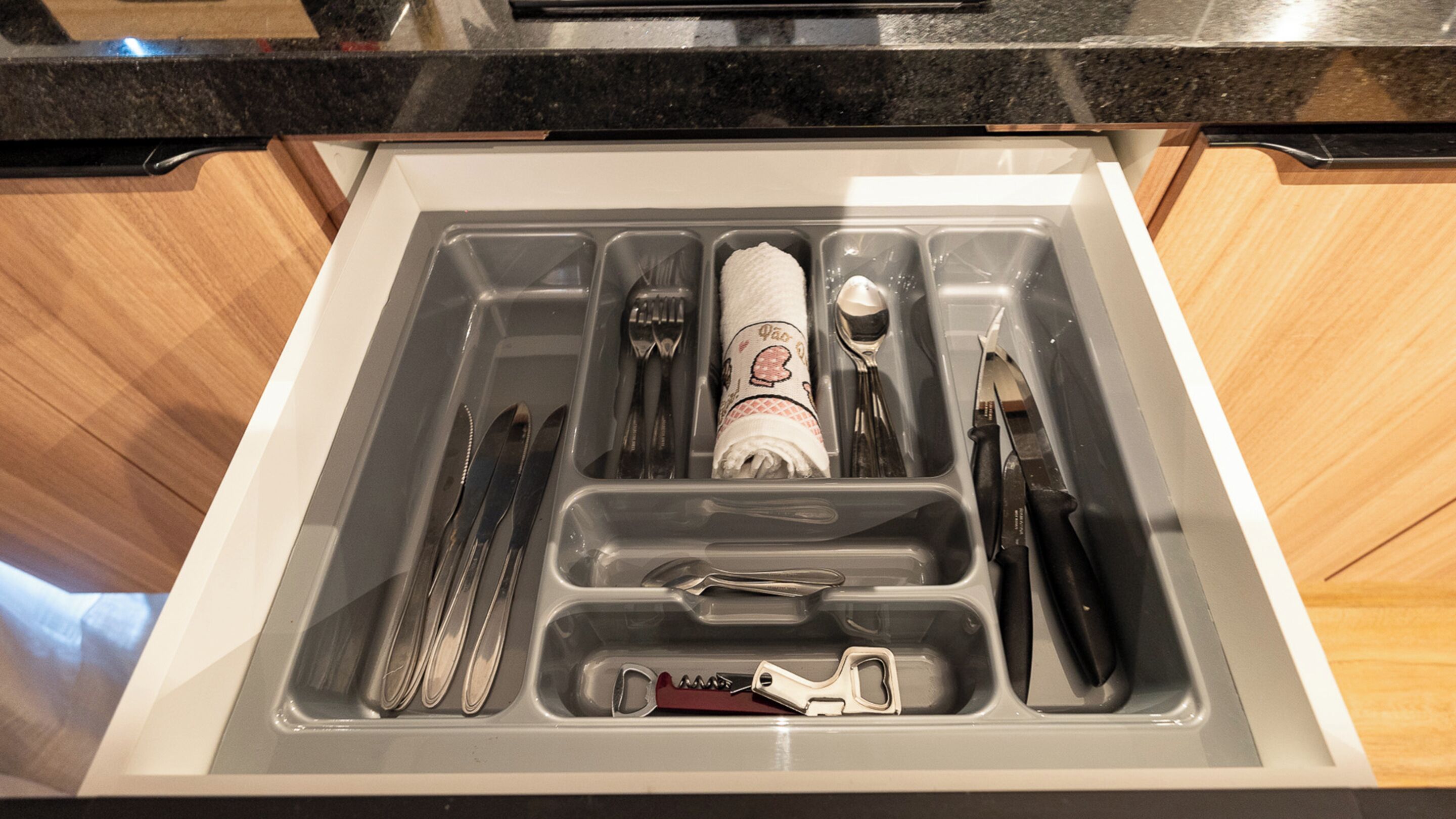 A drawer with utensils, a napkin, and a bottle.