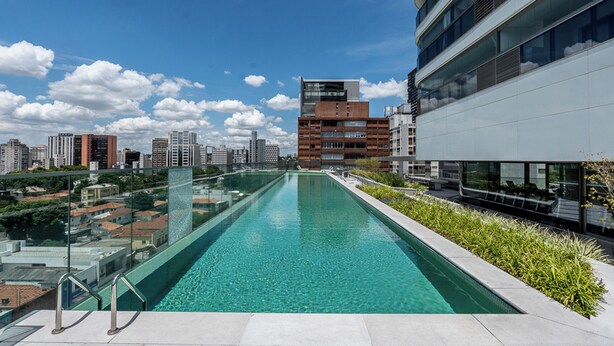 Une piscine sur le toit, avec une eau d’un bleu cristallin, entourée de bâtiments modernes et de verdure.