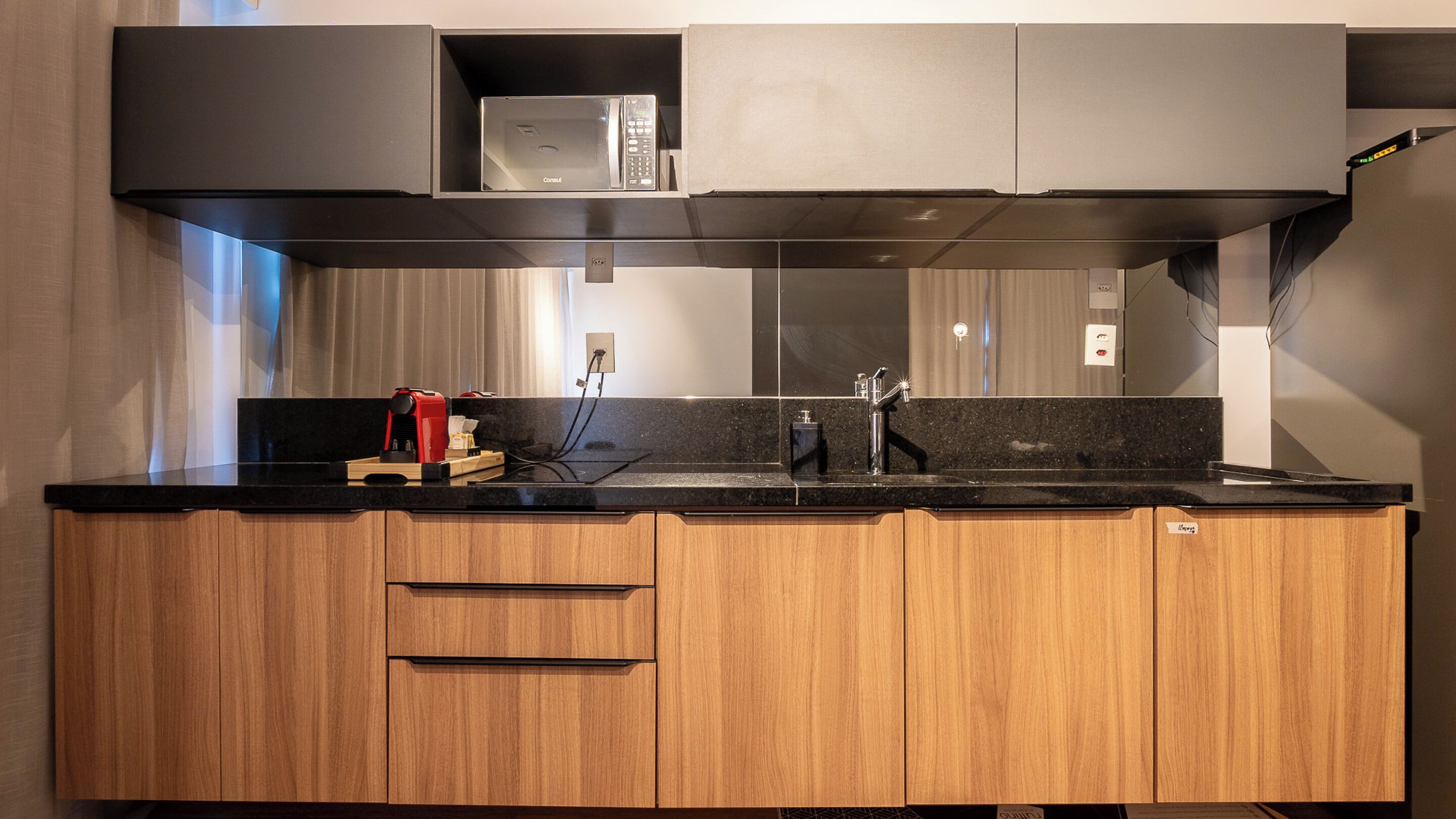 Une cuisine moderne avec des meubles en bois, un plan de travail noir, une machine à café et un four à micro-ondes.