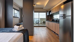 Une chambre d’hôtel moderne comprenant un lit, une salle de bain, un coin cuisine et un balcon avec une chaise.