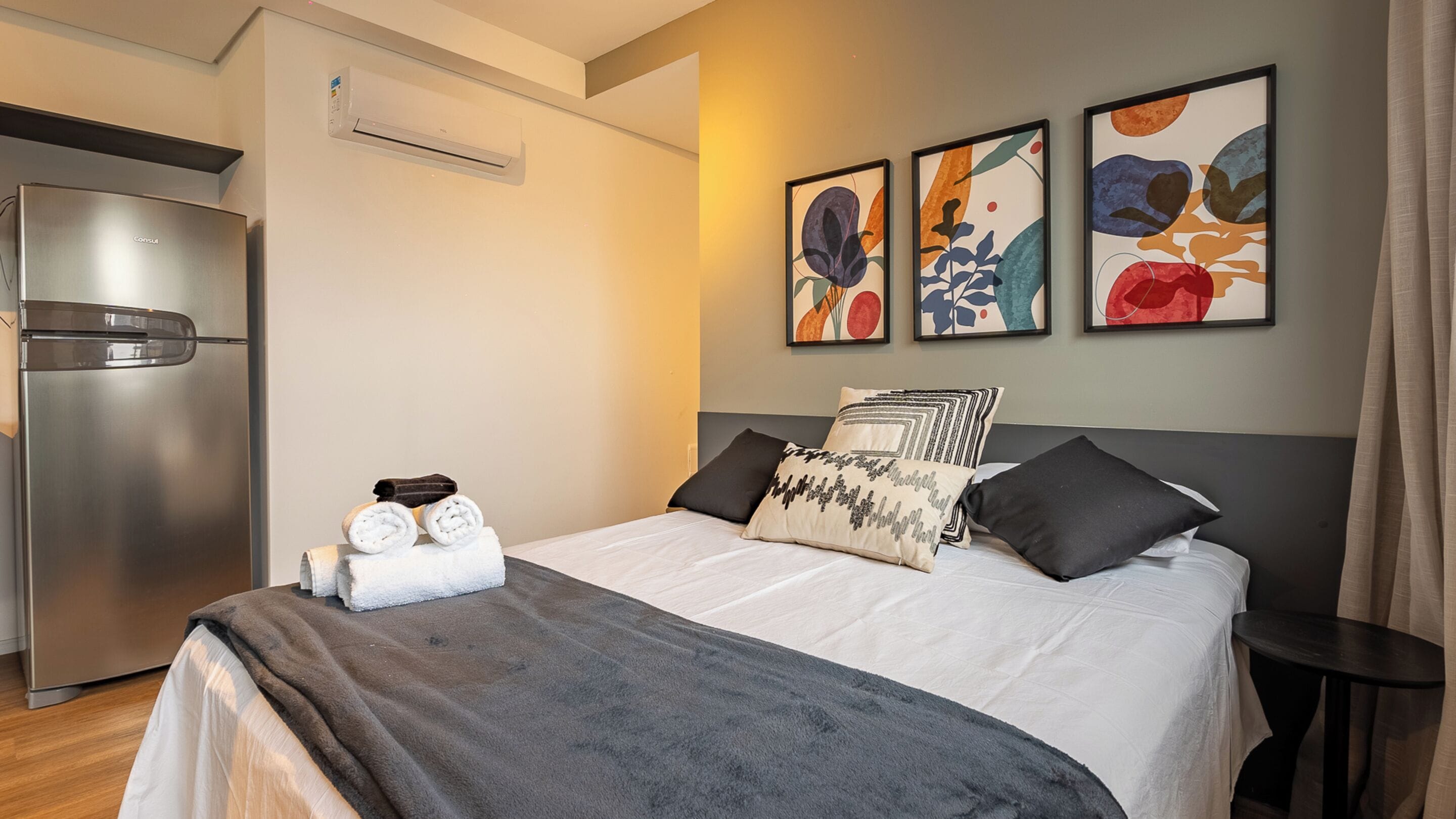 A modern hotel room with a bed, a small table, and a refrigerator.