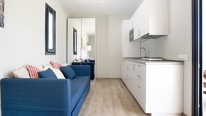 A modern living room with a blue sofa, a kitchen with white cabinets, and a large mirror. - Beautiful Villa for 12 Guests – Adults Only (25+) with Private Pool, Wi-Fi & Air Conditioning (Chiclana de la Frontera)