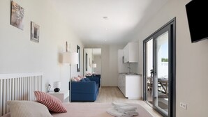 A modern hotel room with a bed, a blue sofa, a small kitchenette, and a sliding glass door to the outside. - Beautiful Villa for 12 Guests – Adults Only (25+) with Private Pool, Wi-Fi & Air Conditioning (Chiclana de la Frontera)