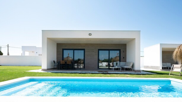 A modern house with a swimming pool, large glass doors, and outdoor seating. - Beautiful Villa for 12 Guests – Adults Only (25+) with Private Pool, Wi-Fi & Air Conditioning (Chiclana de la Frontera)