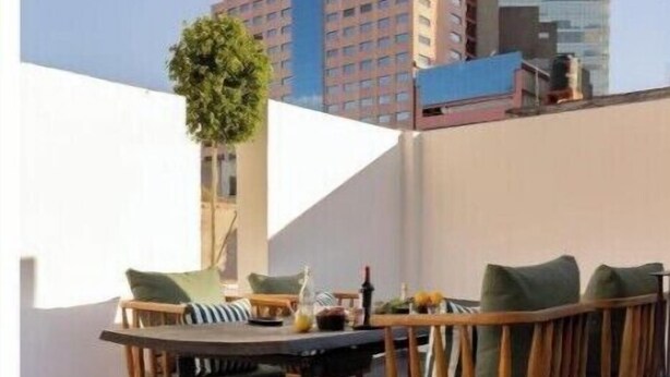 Een terras op het dak met een eettafel en stoelen, een potplant en een uitzicht op het stadsbeeld van Barcelona.