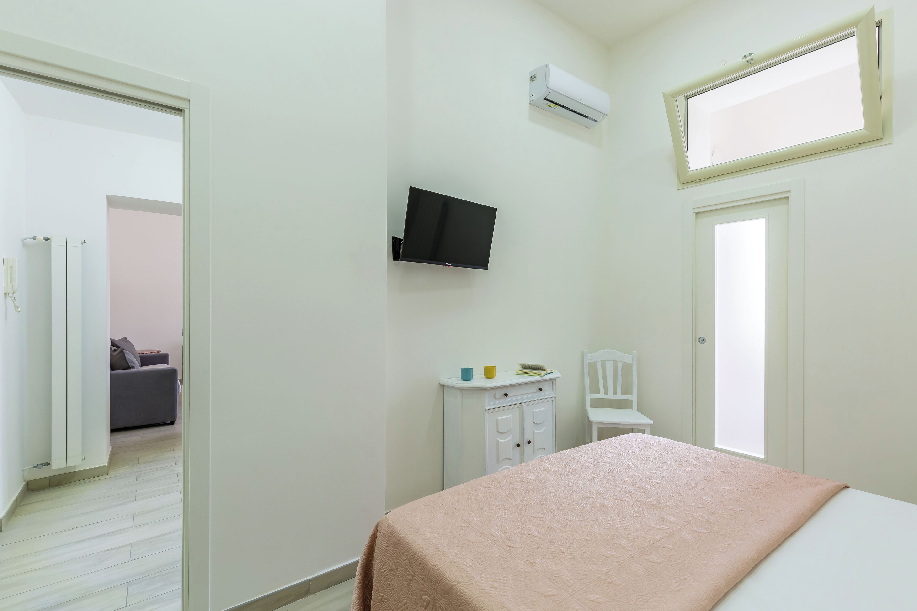 A bedroom with a bed, a television, a small cabinet, and a window.