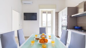 A modern kitchen with a dining area, featuring a table set with orange juice, a plate of oranges, and a pie.