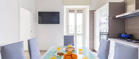 A modern kitchen with a dining area, featuring a table set with orange juice, a plate of oranges, and a pie.