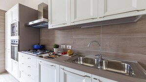 A modern kitchen with white cabinetry, a stainless steel sink, a built-in oven, and a blue pot on the stove.
