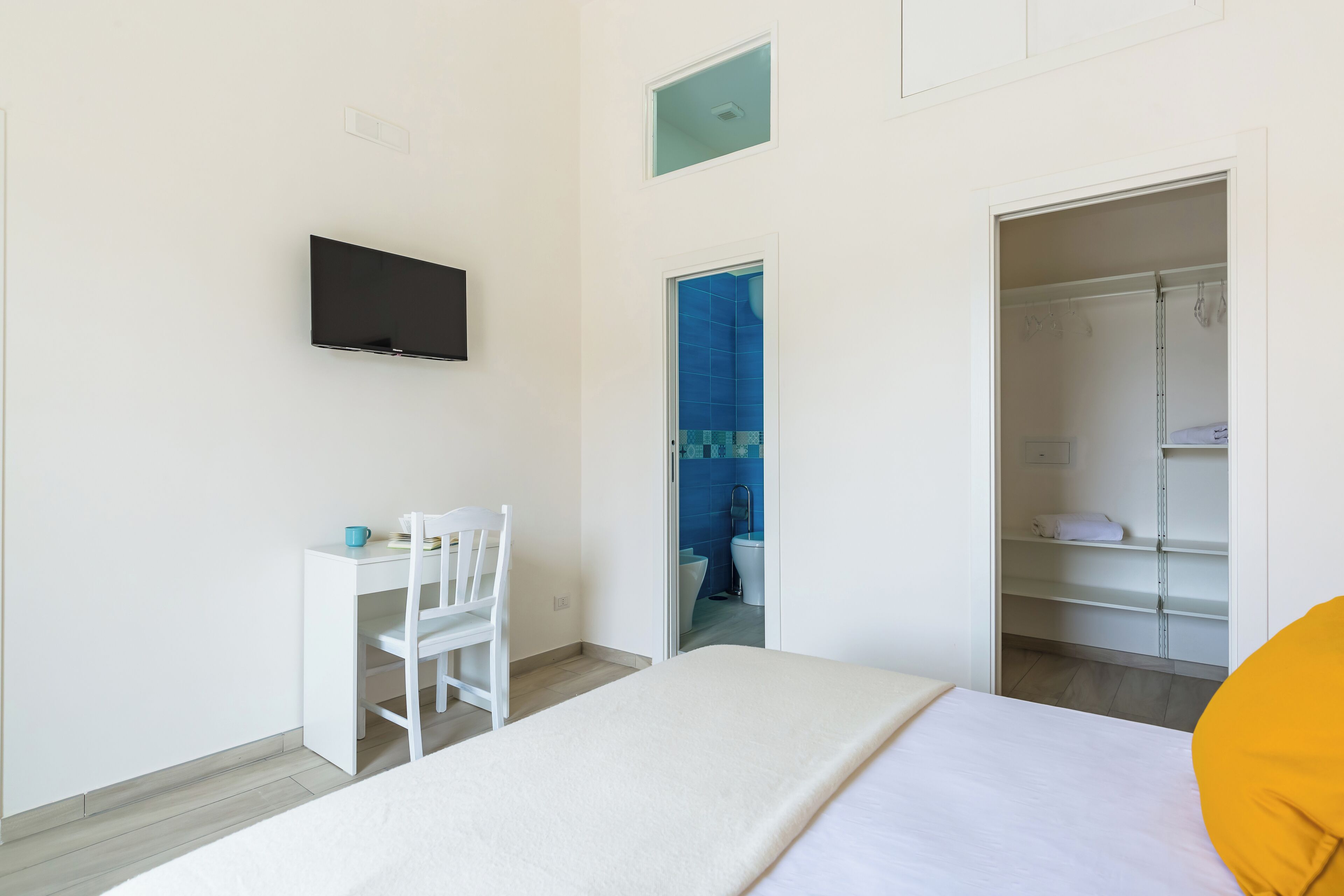 A bedroom with a bed, a desk, a chair, a TV, and a wardrobe.