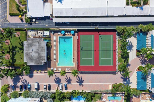 Vista aérea de un complejo turístico con piscina, canchas de tenis y zona de estacionamiento.