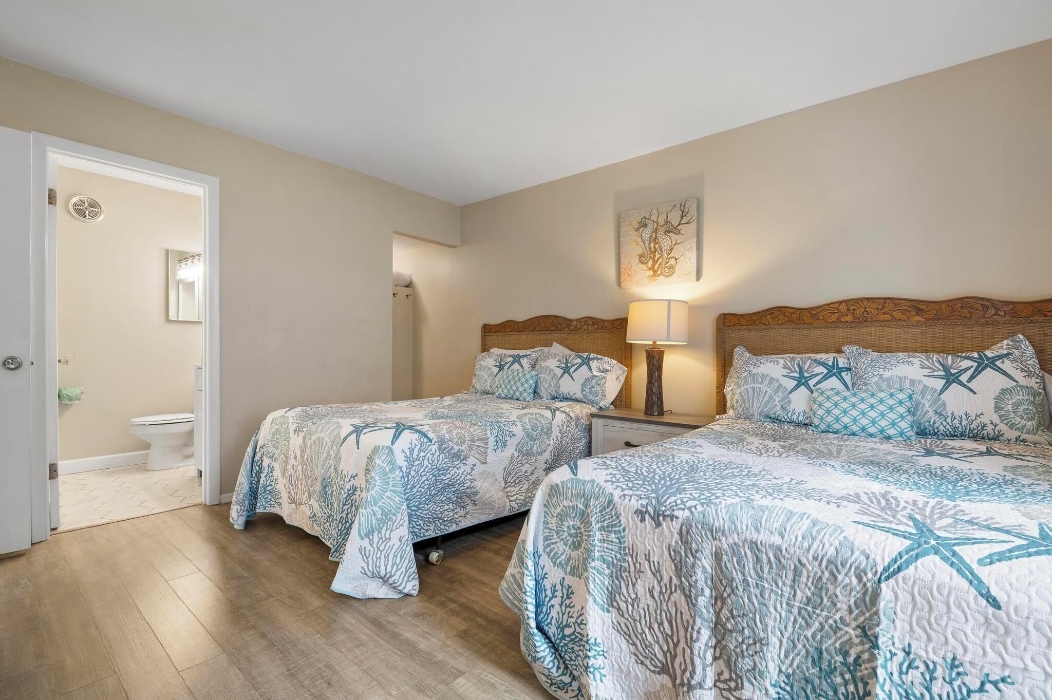 A bedroom with two beds, a nightstand, a lamp, and a door leading to a bathroom.