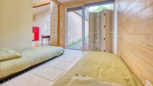 Une chambre avec deux lits, un plancher en bois, un appareil électroménager rouge et une porte-fenêtre coulissante donnant sur l’extérieur.