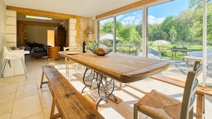 Un vaste espace dédié à la salle à manger, avec une grande table en bois, des chaises en osier et une vue sur un jardin luxuriant grâce à de grandes fenêtres.