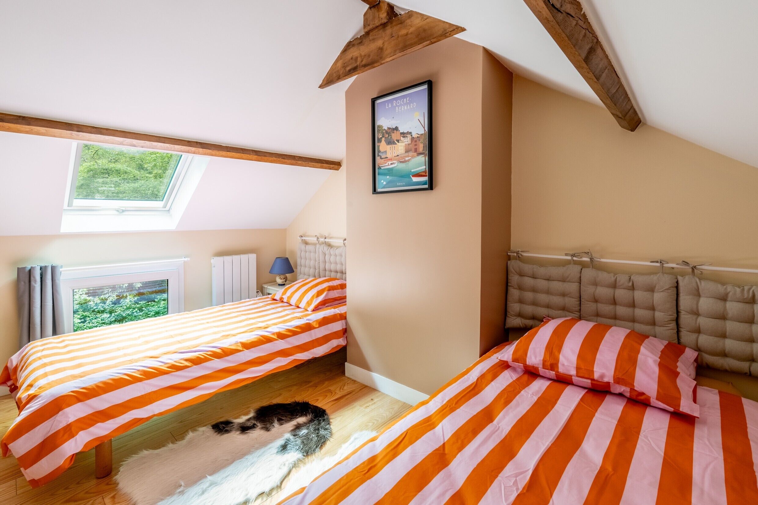 A bedroom with two beds, a window, a framed picture, and a wooden ceiling beam.