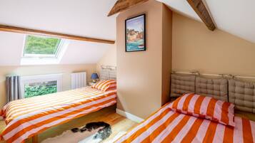 A bedroom with two beds, a window, a framed picture, and a wooden ceiling beam.