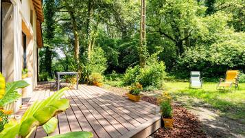 A wooden deck with potted plants, a table, and chairs, surrounded by lush greenery and trees.