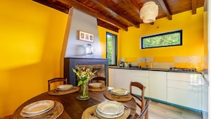 A dining area with a wooden table set for six, a fireplace, and a kitchen adjacent to the dining area.