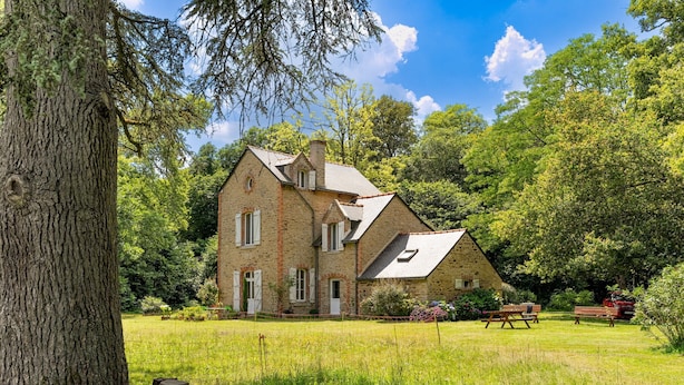 A stone house with a sloped roof, surrounded by a grassy yard and trees.