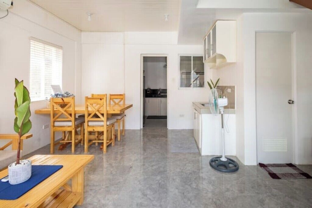 Una habitación amplia con una mesa de comedor de madera y sillas, una planta pequeña y un armario blanco con un ventilador.
