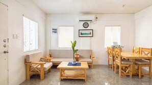 A room with a sofa, a wooden table, and a dining table with chairs. There is a clock on the wall and a plant on the table. - Serene Cozy Air Con Home in Fully-Secured Complex (Urdaneta city)
