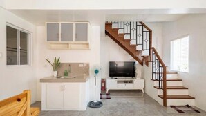 A compact living space with a kitchenette, a TV, a wooden staircase, and a small seating area. - Serene Cozy Air Con Home in Fully-Secured Complex (Urdaneta city)