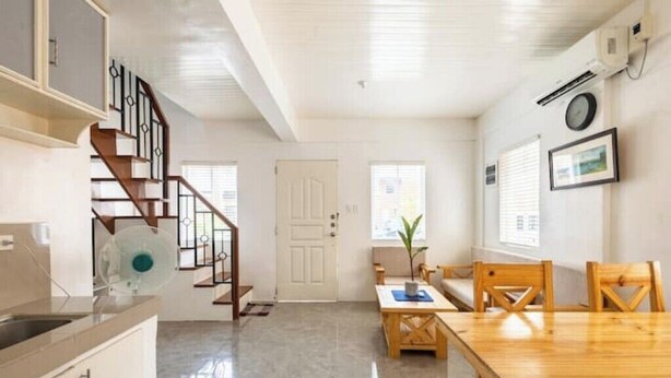 A spacious kitchen with a wooden staircase, a dining area with a wooden table and chairs, and a white door. - Serene Cozy Air Con Home in Fully-Secured Complex (Urdaneta city)